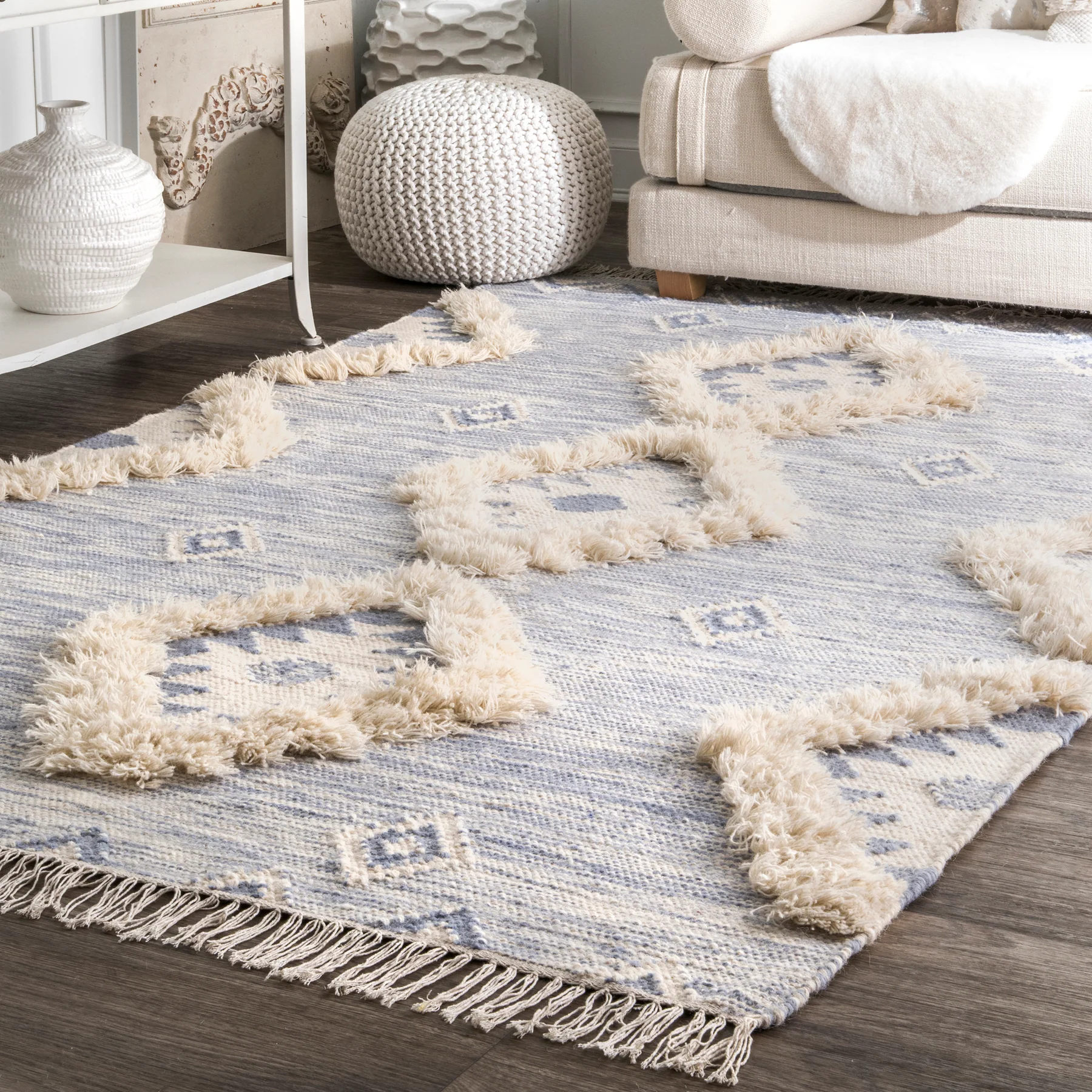 An area rug with a blue base, decorated with raised beige geometric patterns and tassels along the edges.