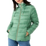 A woman is wearing a light green quilted puffer jacket with a high collar and hood, paired with blue jeans.