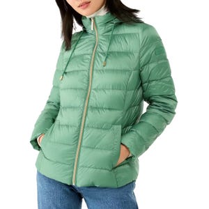 A woman is wearing a light green quilted puffer jacket with a high collar and hood, paired with blue jeans.