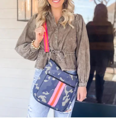 A camouflage patterned messenger bag with a blue background and pink and red stripes across the front, featuring a bright pink strap.