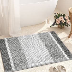A plush, grey-striped chenille bath mat situated on a bathroom floor, accompanied by a tub, a bouquet of flowers, a champagne glass, and slippers, creating a cozy and elegant atmosphere.