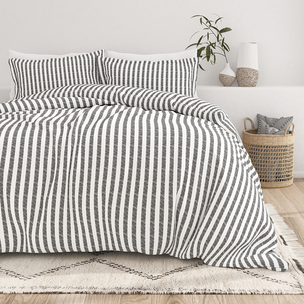 A bed with a black and white vertical striped duvet and pillows is set in a minimalist bedroom. A woven basket and decorative vases complete the decor.