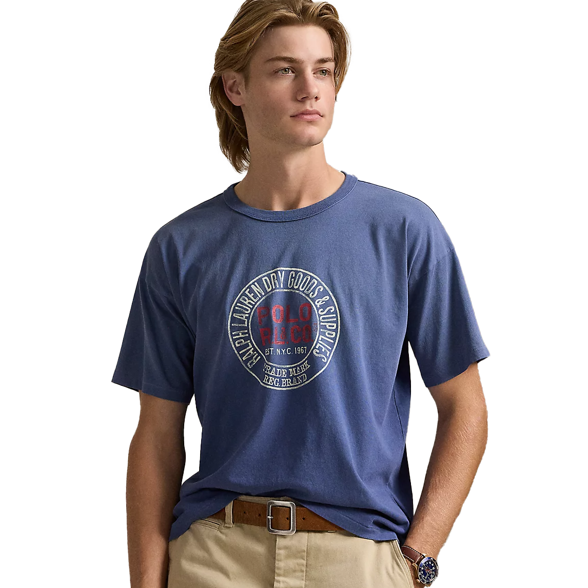 A blue short-sleeve Polo Ralph Lauren tee featuring a circular graphic with \“Polo R.L.C.O\“ and \“Ralph Lauren Dry Goods & Supplies\“ text. The design includes \“Est. NYC 1967\“ and \“Trade Mark Reg. Brand.\“