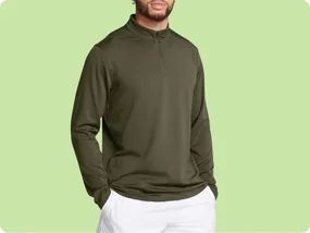A person is wearing a long-sleeve, olive green, half-zip pullover sweater paired with white pants against a light green background.