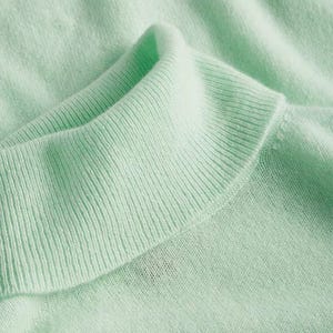 A light green cashmere turtleneck sweater with a soft, ribbed collar, designed for comfort and warmth.