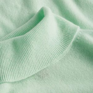 A light green cashmere turtleneck sweater with a soft, ribbed collar, designed for comfort and warmth.