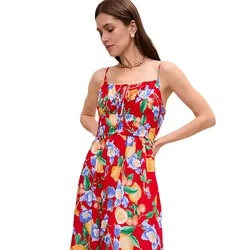 A woman wears a vibrant red sundress with blue and orange floral patterns, featuring spaghetti straps and an elasticated waist.
