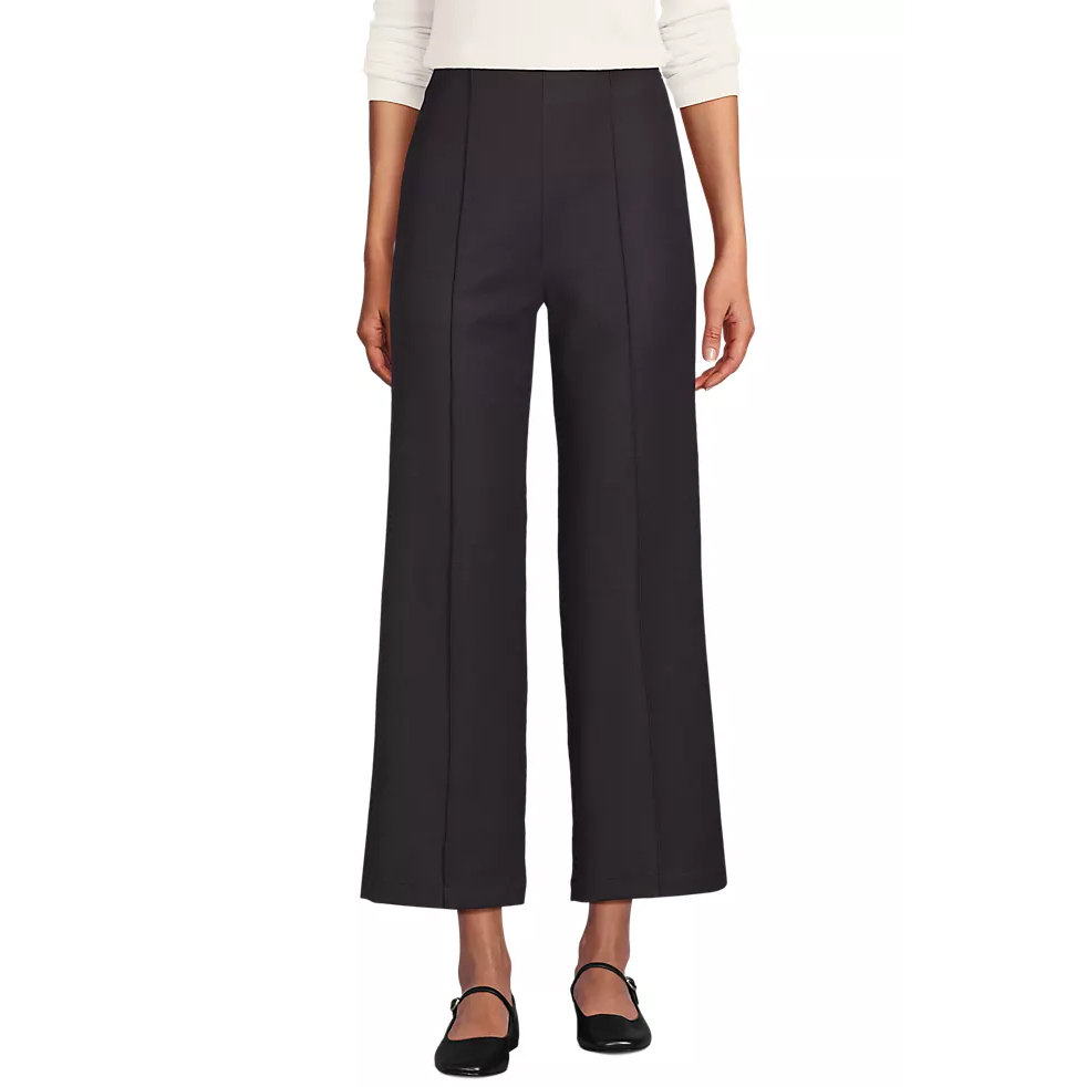Black wide-leg pants with front seam details, paired with black Mary Jane shoes and a white long-sleeve top.