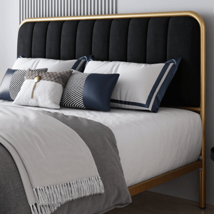 A bed with a black upholstered headboard featuring a gold frame, adorned with white and navy pillows, including one with a distinctive geometric pattern, and a gray blanket with fringe detailing.