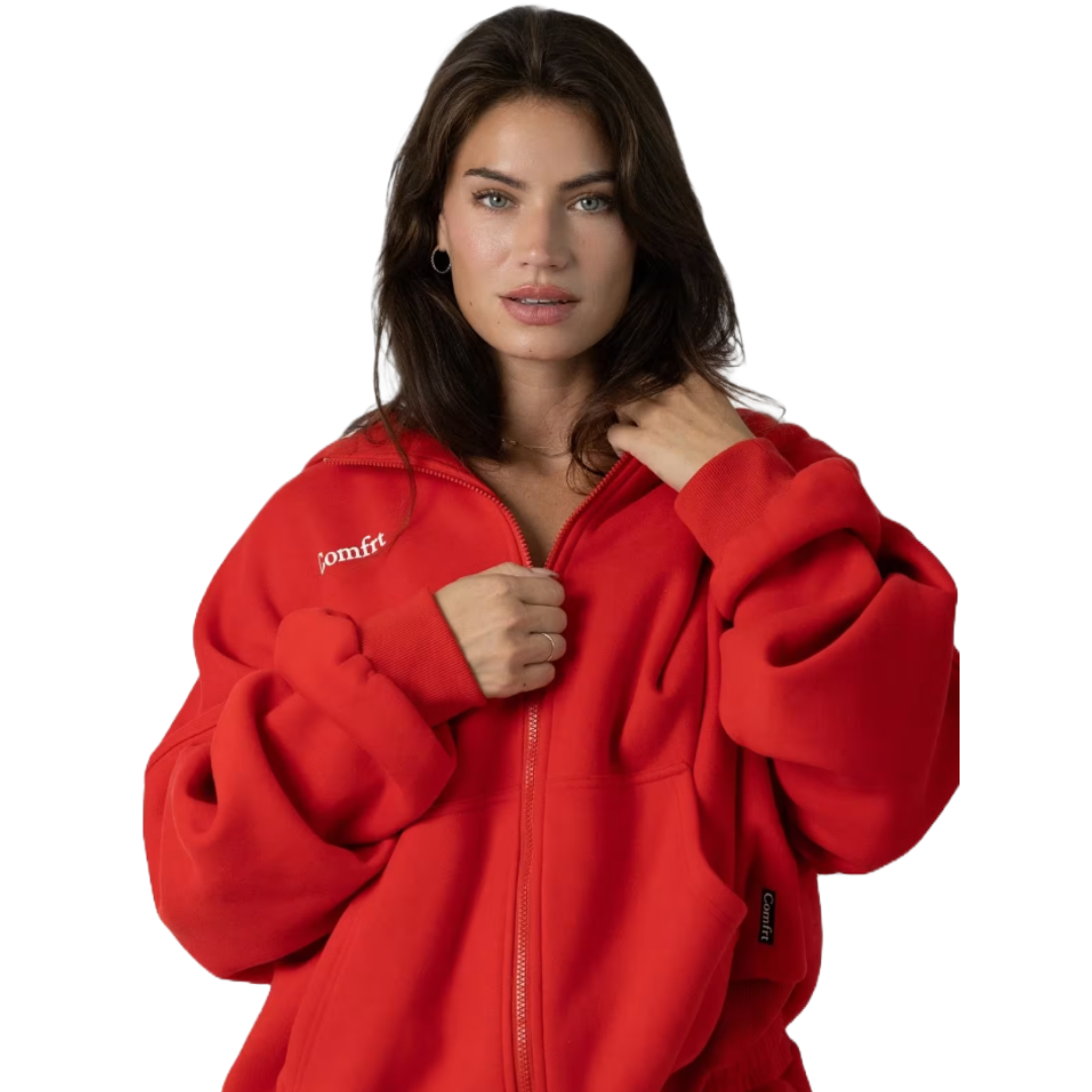 A person wears a bright red zip-up hoodie with \“comfrt\“ written on it, featuring a relaxed fit and adjustable hood.