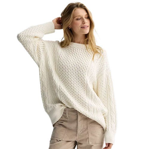 A woman is wearing a cream-colored, textured knit sweater with loose, relaxed cuffs, paired with beige pants.