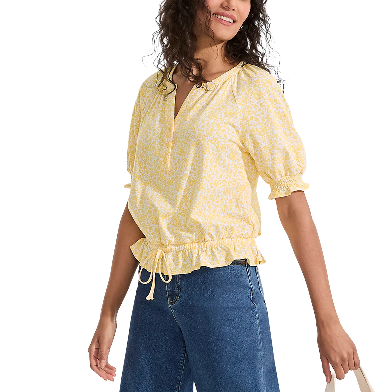 A woman wears a yellow floral blouse with puff sleeves, a v-neck, and a drawstring waist, paired with blue jeans.