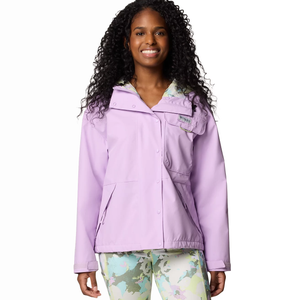 A woman is wearing a Columbia Hooded Rain Jacket in light purple with a front pocket and snap closures, complemented by colorful patterned pants.