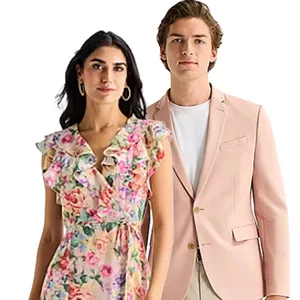 A woman in a floral ruffle dress stands next to a man in a light pink blazer and white shirt.