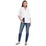 A woman is wearing a white button-up shirt, blue skinny jeans, and light blue flat shoes.