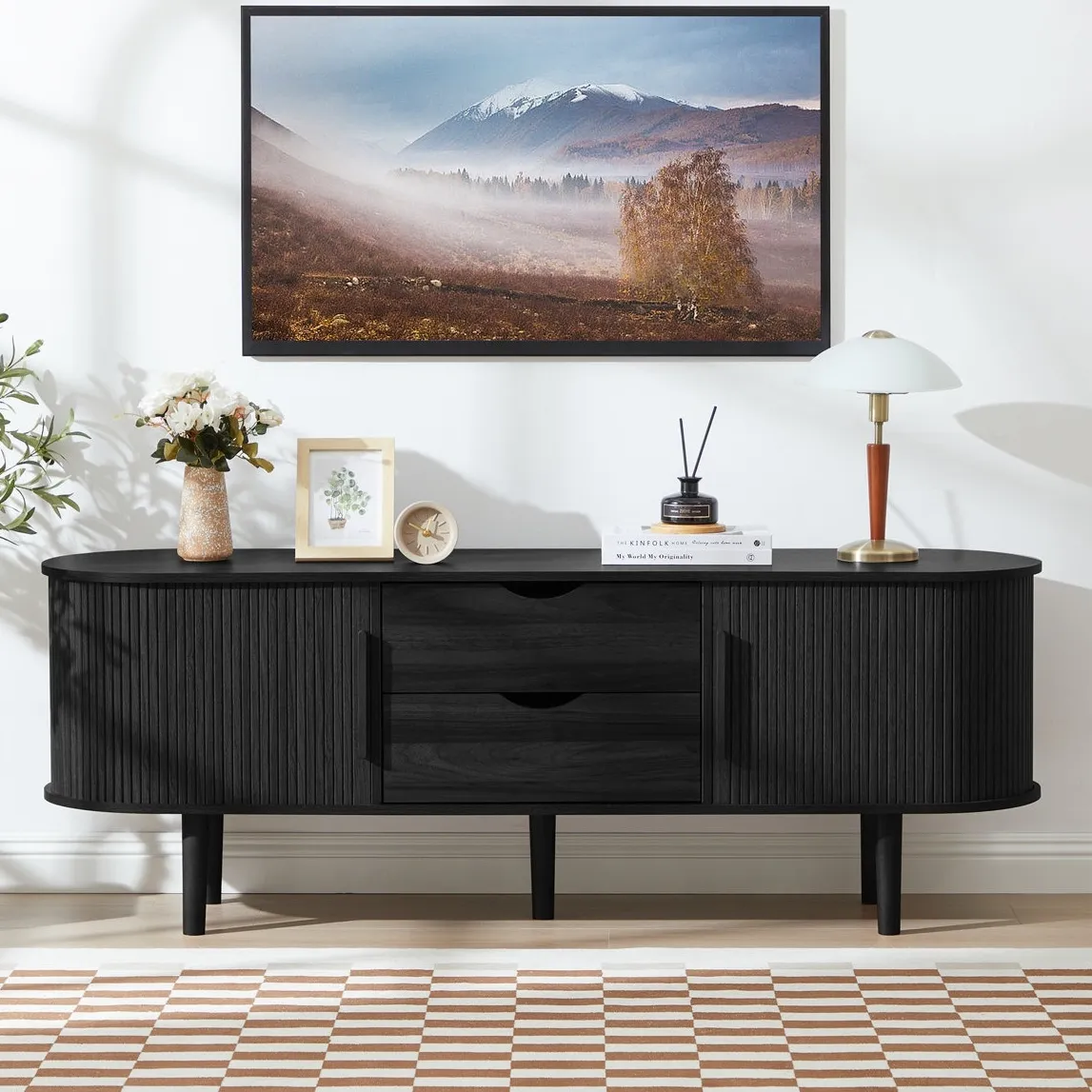 Black wooden sideboard with curved edges, featuring drawers and cabinets, topped with a landscape artwork, decorative items, and a lamp. A checkered rug and plant complete the modern decor.