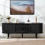 Black wooden sideboard with curved edges, featuring drawers and cabinets, topped with a landscape artwork, decorative items, and a lamp. A checkered rug and plant complete the modern decor.