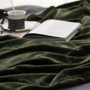 A soft green blanket is draped beside an open book and a coffee cup on a saucer, creating a cozy setting.