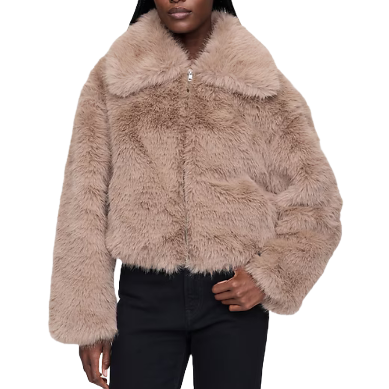 A person wearing a fluffy beige jacket with a collar, paired with black pants.