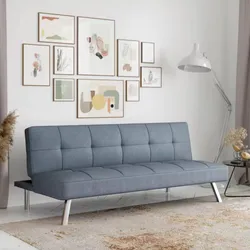 Modern living room features a blue futon-style sofa with chrome legs, artistic wall gallery with abstract prints, a tall white floor lamp, and a round side table with decorative elements, set on a neutral-patterned rug.