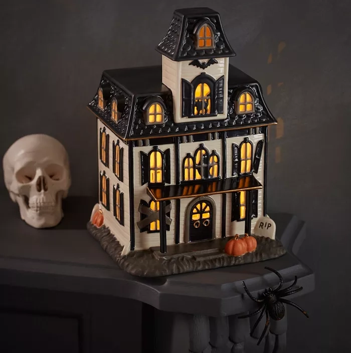 A decorative haunted house with illuminated windows, alongside a skull and spider.