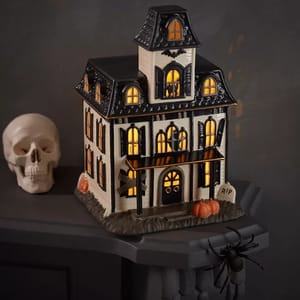 A decorative haunted house with illuminated windows, alongside a skull and spider.