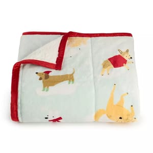 A cozy throw blanket featuring playful dog illustrations, including a dachshund in a Santa hat and a corgi in a red sweater, set against a soft, light-colored background with a plush red trim.