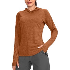 A lightweight, long-sleeved hoodie in a rust color, designed for sun protection, features a subtle heathered texture. It offers a relaxed fit with a slightly curved hem, paired with gray pants.