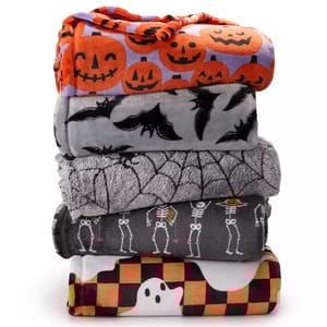 A stack of Halloween-themed blankets featuring designs with jack-o'-lanterns, bats, spiderwebs, skeletons, and ghosts on a checkered background.