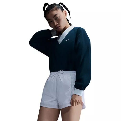 Nike Women's Woven V-Neck Top features a dark navy design with a white collar and logo, providing a classic, sporty look. It's paired with white shorts, creating a stylish contrast.