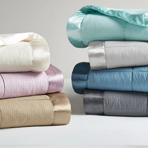 Piles of folded bed sheets in various colors including white, pink, blue, and grey.