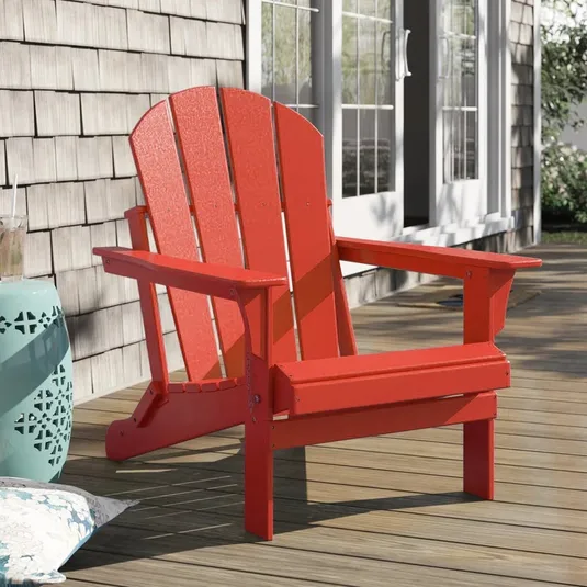 A red Adirondack chair on a wooden deck.