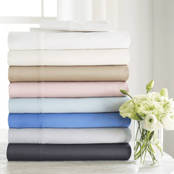 A stack of folded bed sheets in various colors, accompanied by a vase of white flowers.