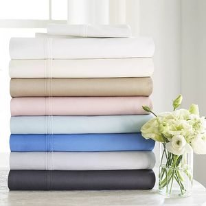 A stack of folded bed sheets in various colors, accompanied by a vase of white flowers.