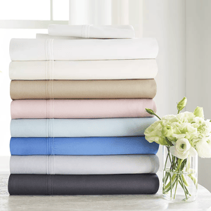 A stack of folded bed sheets in various colors, accompanied by a vase of white flowers.