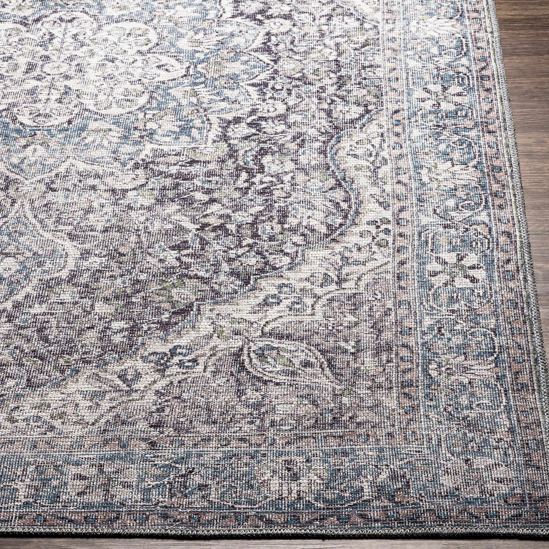 A 9' x 12' machine-washable area rug featuring a vintage-inspired design with a mix of blue, gray, and cream tones, showcasing intricate floral and medallion patterns on a bordered edge.