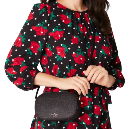Person wearing a black dress with red floral and white polka dot pattern, holding a small black crossbody bag.
