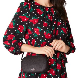 Person wearing a black dress with red floral and white polka dot pattern, holding a small black crossbody bag.