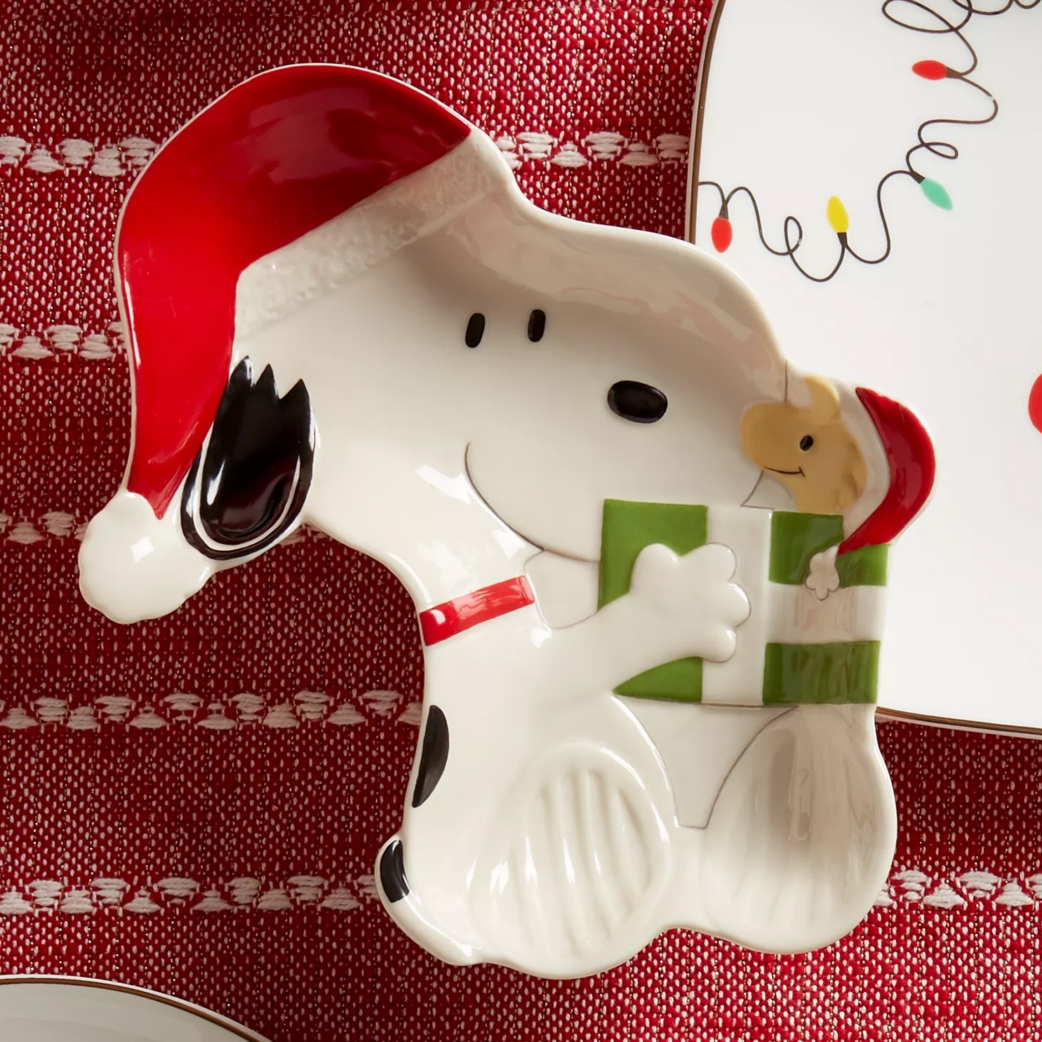 Ceramic dish shaped like a dog with a Santa hat, holding a green gift. Set against a red, textured background.