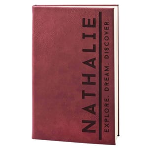 A burgundy notebook with the name \“Nathalie\“ in large vertical letters and the phrase \“Explore. Dream. Discover.\“ written horizontally.