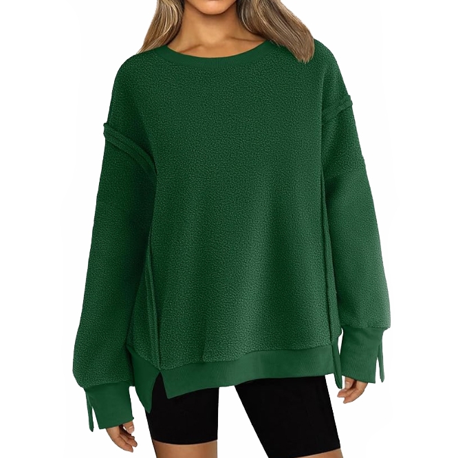 A woman is wearing a dark green oversized sweater paired with black shorts. The sweater features long sleeves and a relaxed fit.