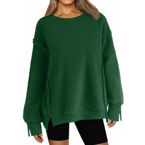 A woman is wearing a dark green oversized sweater paired with black shorts. The sweater features long sleeves and a relaxed fit.