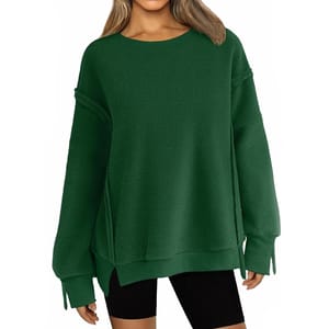 A woman is wearing a dark green oversized sweater paired with black shorts. The sweater features long sleeves and a relaxed fit.