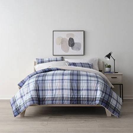 A bed with blue and white plaid bedding set, accompanied by a wooden nightstand and a black desk lamp.