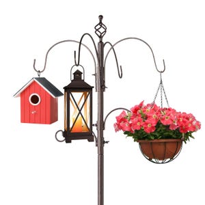 A multi-hook garden pole features a hanging red birdhouse, a black lantern with a light, and a pot of pink flowers.