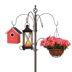 A multi-hook garden pole features a hanging red birdhouse, a black lantern with a light, and a pot of pink flowers.