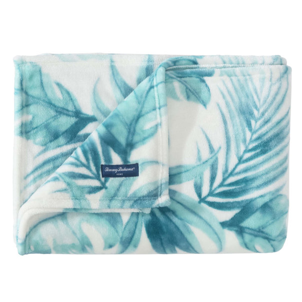 A Tommy Bahama beach-themed throw with a tropical leaf design in shades of teal and white. The plush fabric features a soft texture, ideal for cozy settings.