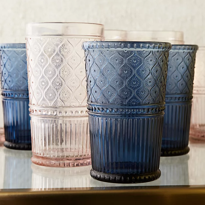 A set of embossed glass tumblers in assorted colors such as blue and pink, displayed on a reflective surface.