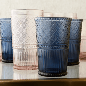 A set of embossed glass tumblers in assorted colors such as blue and pink, displayed on a reflective surface.