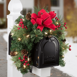 A festive mailbox swag adorned with pine branches, red berries, pinecones, a large red ribbon, and twinkling lights, creating a holiday-themed decoration for a mailbox.